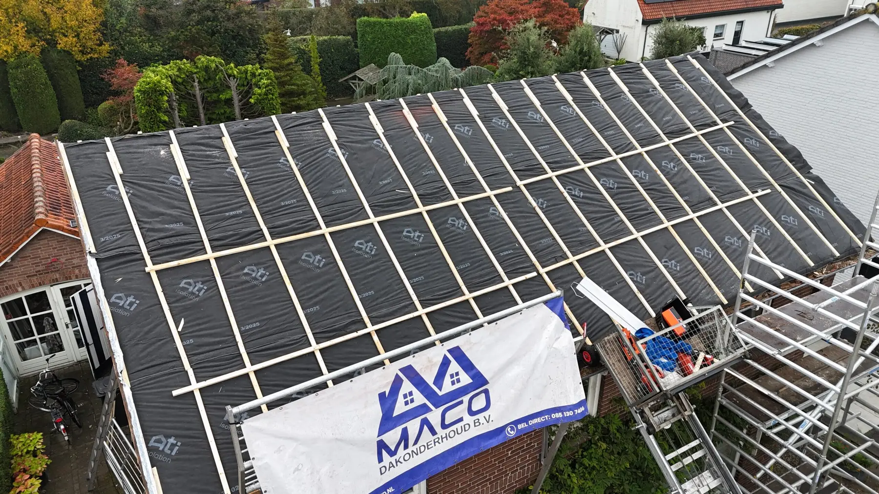 Dronefoto van een dakrenovatie met het spandoek van MACO Dakonderhoud op de steiger